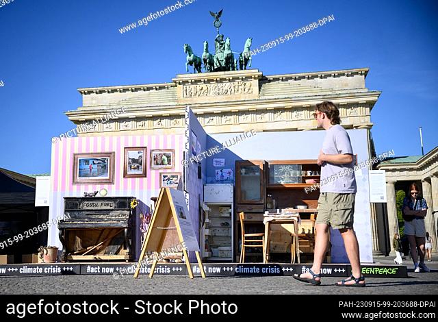 15 September 2023, Berlin: Passers-by look at a replica of a flood-damaged apartment in front of the Brandenburg Gate, which Greenpeace is using to protest for...