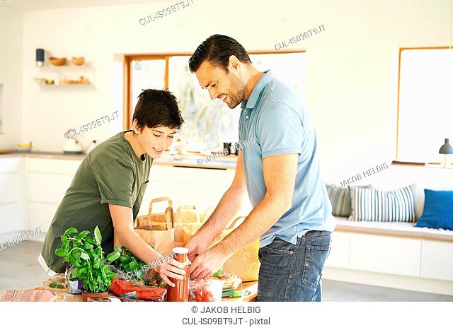 Boy and his father at kitchen counter unpacking groceries