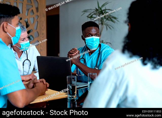 Diverse male and female doctors wearing face masks sitting in hospital having discussion