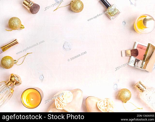 Holiday feminine cosmetic background in golden colour. Cosmetic objects frame with gold heels, christmas balls, gold glitter nail polish, perfume bottle