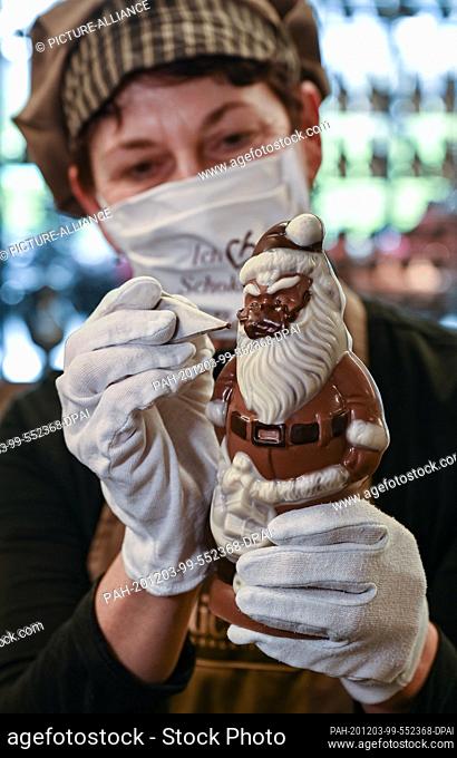 02 December 2020, Brandenburg, Hornow: Anne Walter, chocolatier from the Confiserie Felicitas, uses liquid chocolate to decorate a little Santa Claus with a...