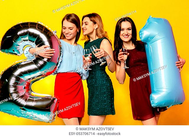 21th Happy birthday anniversary. Three amazing pretty girls having fun while celebrating a holiday with balloons, isolated over yellow background