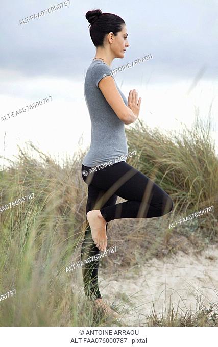 Mature woman in tree pose on beach, side view