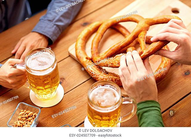 people, leisure and drinks concept - close up of men drinking beer with pretzels at bar or pub