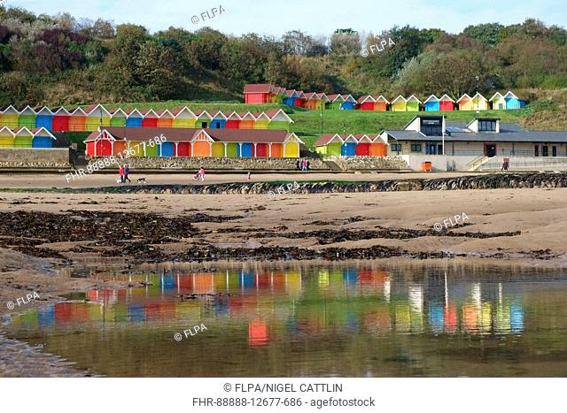 Colourful beach huts reflected in pools on beach at low tide, North Bay, Scarborough, England, October