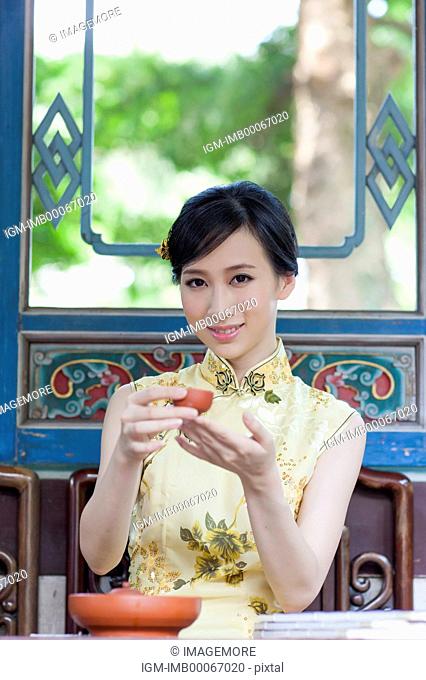 Young woman with cheongsam holding a cup of tea and smiling at the camera