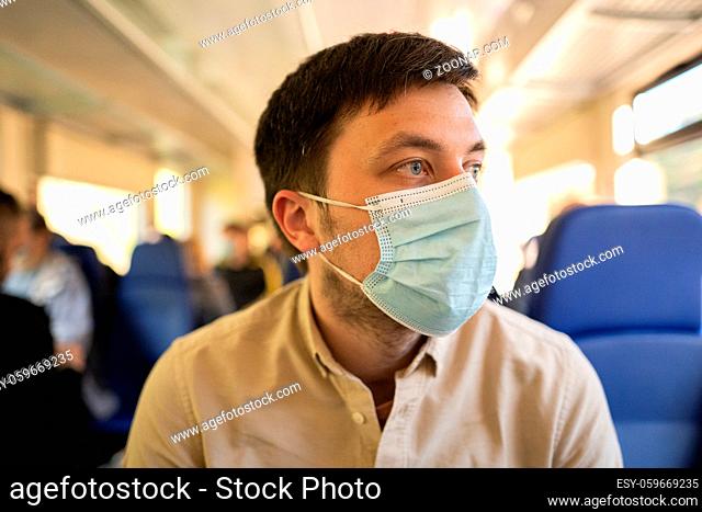 Man traveling by train wearing a facemask. Social distancing when traveling by railway during Covid-19 pandemic. Male commute to work in public transport train...