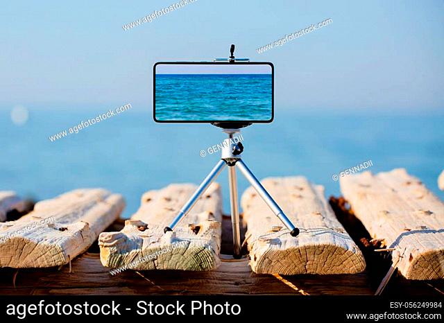 Smartphone on tripod making photo and video of beautiful sea landscape