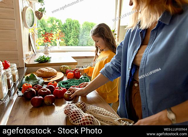 Mother and daughter unpacking fresh groceries in kitchen
