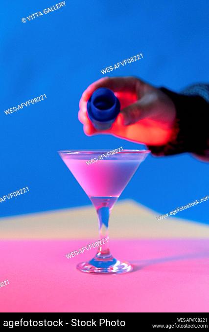 Hand of man pouring blue liquid into martini glass with pink liquid
