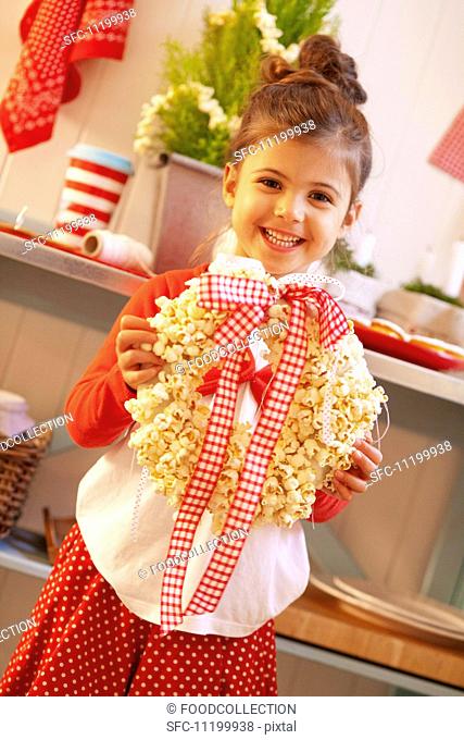 A small girl holding a Christmas wreath made from popcorn