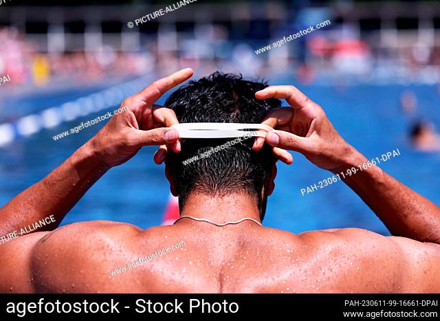 11 June 2023, North Rhine-Westphalia, Cologne: Payam from Cologne puts on his swimming goggles at the edge of the pool in Cologne's Stadionbad to swim a few...