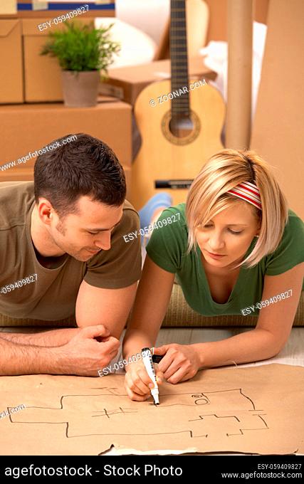 Young couple lying on floor of new house planning home together on paper