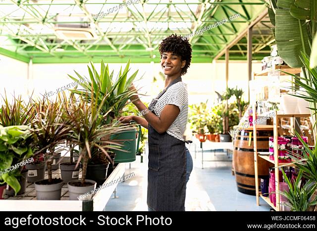 Smiling gardener holding watering can standing near plants at nursery