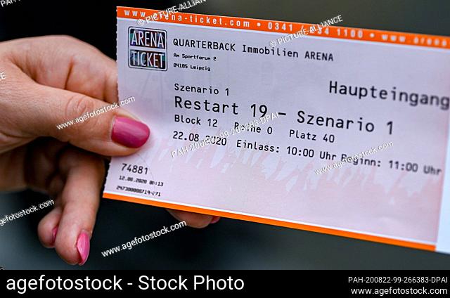 22 August 2020, Saxony, Leipzig: A test person of a large-scale experiment of the University Medicine Halle/Saale holds a concert ticket in her hand in front of...