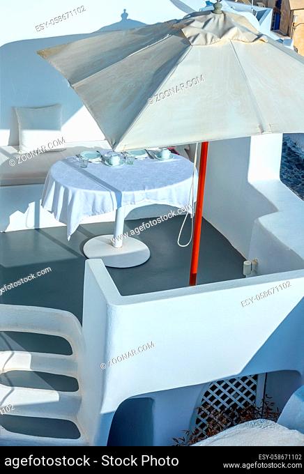 Greece. Sunny summer day on the caldera of Santorini island. Served table under a sun umbrella on the outdoor terrace