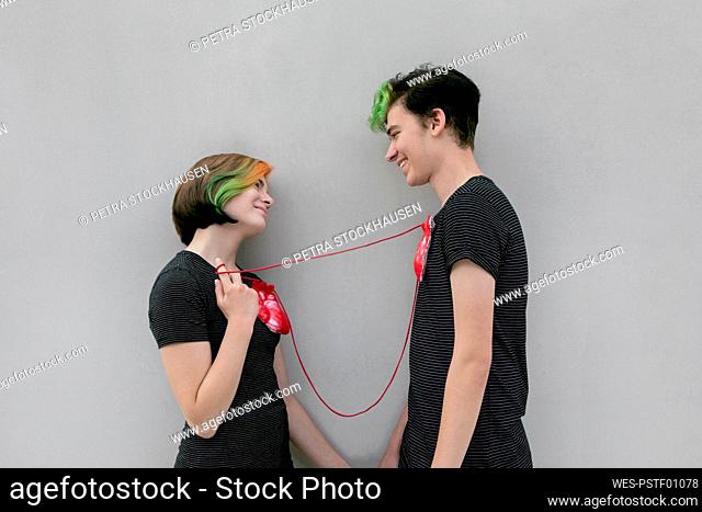Teenage couple connected hearts with rope against gray background