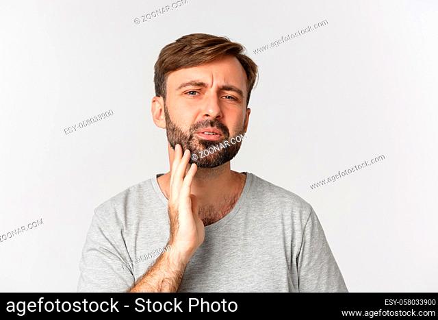 Close-up of confused man touching his beard and looking at himself, need to shave, standing over white background