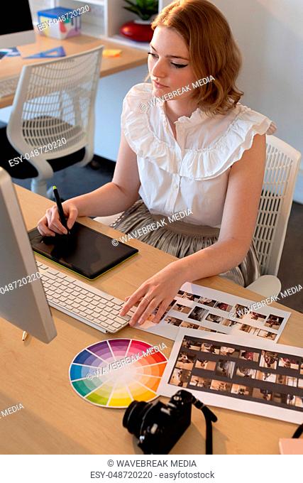 Female graphic designer working on graphics tablet and computer at desk