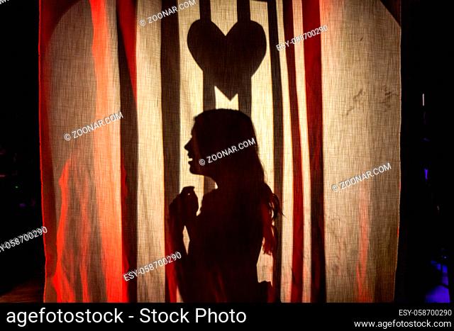 A girl is seen on stage in a school theater with a heart above her head, casting silhouettes onto a curtain as she plays the damsel