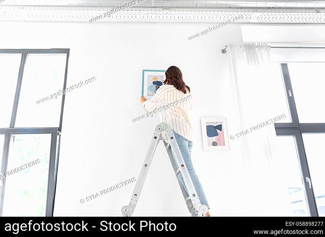 woman on ladder decorating home with art