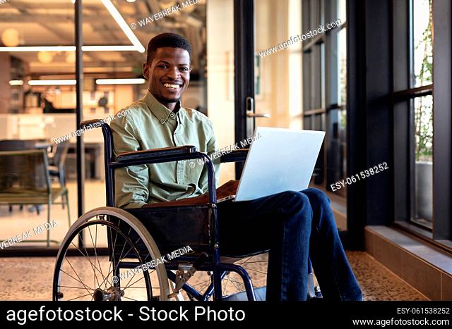 Smiling african american businessman with disability using laptop in wheelchair at workplace