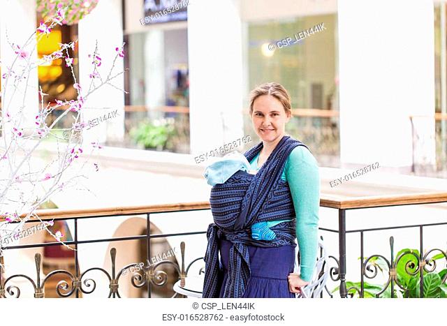 Happy mother walking with her baby in sling