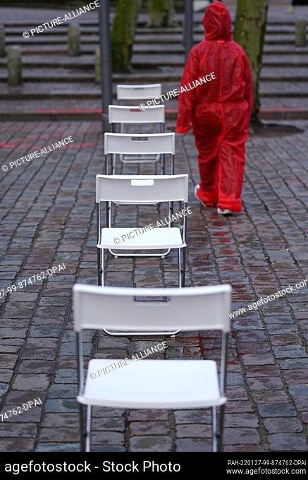 27 January 2022, Hamburg: A woman in a red protective suit walks along white chairs on Gerhart-Hauptmann-Platz in the city center during a performance...