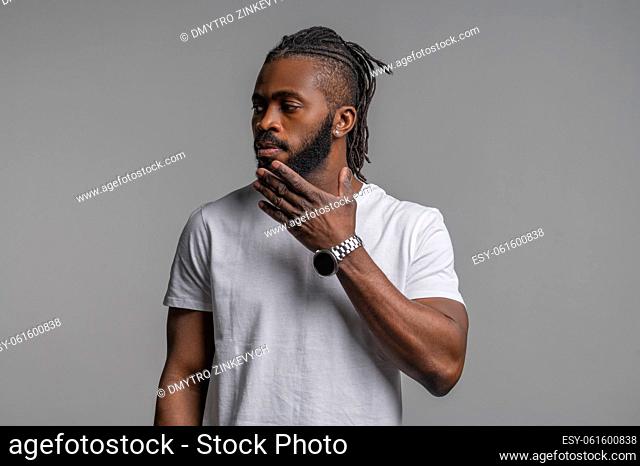 Waist-up portrait of a serious pensive young African American man touching his chin and looking away