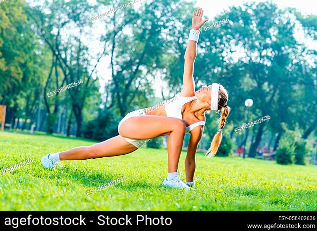 Young fitness girl stretching in park on green grass