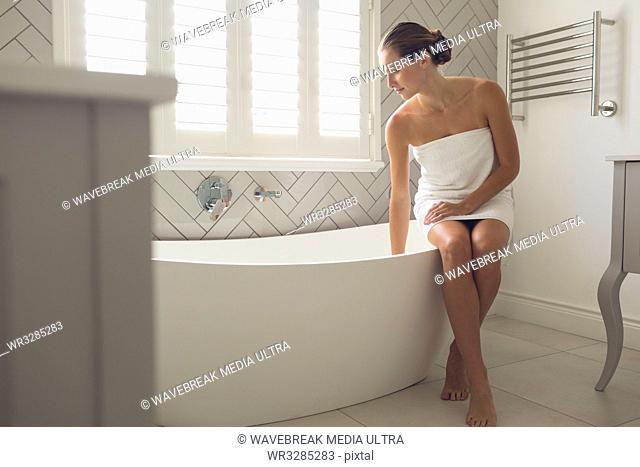 Beautiful woman checking the level of water in the bathtub in bathroom