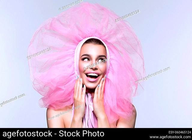 Beautiful happy young woman in fluffy pink headwear with surprised expression. Beauty shot. Over grey background. Copy space