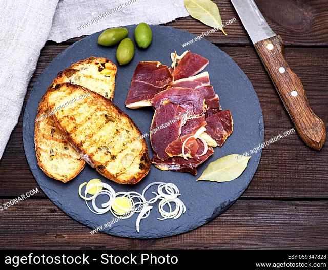 pieces of jamon and white fried bread for a sandwich on a black surface, top view