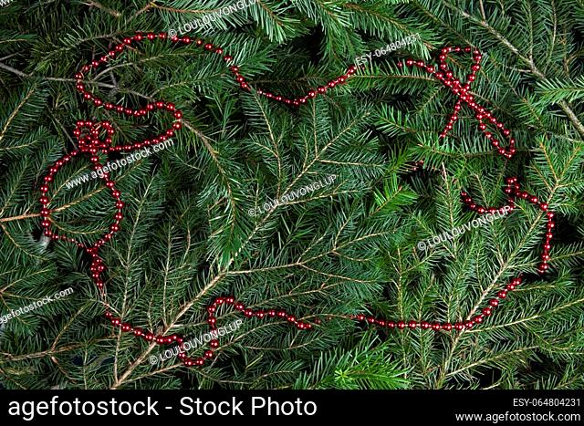 zoom on a pile of fir branches with a frame of bright red pearl garland. Texture for graphic resource