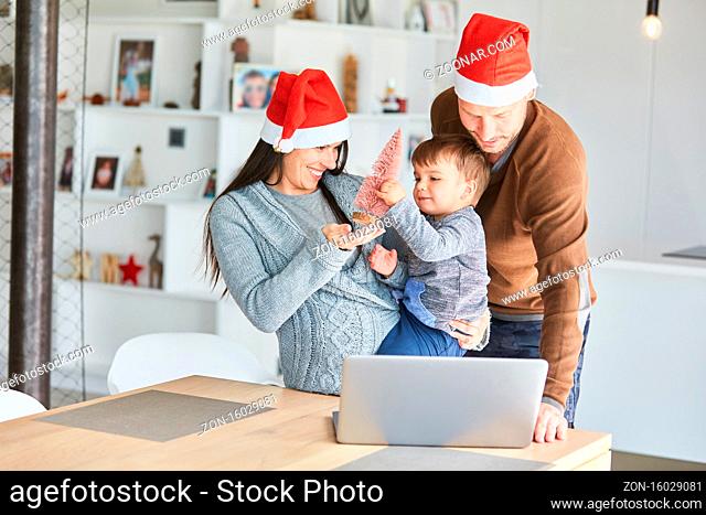 Familie mit Kind auf dem Arm im Wohnzimmer macht einen Videochat zu Weihnachten