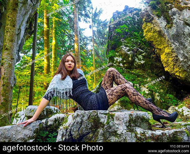 Young woman in nature reclining on big boulder rock looking away