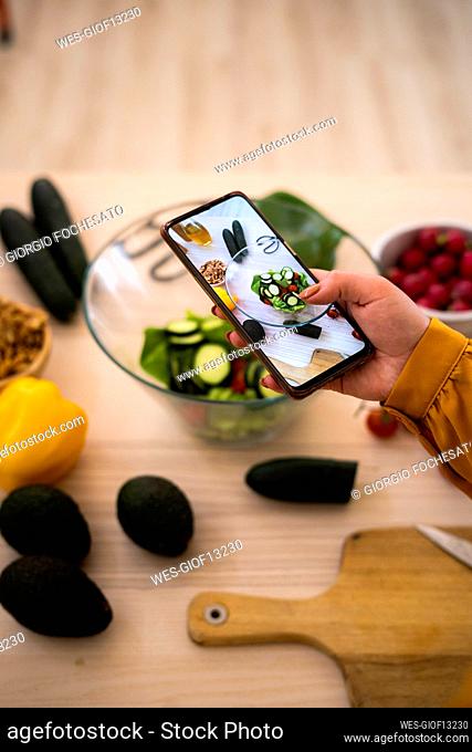 Woman taking photo of vegetables through smart phone at table