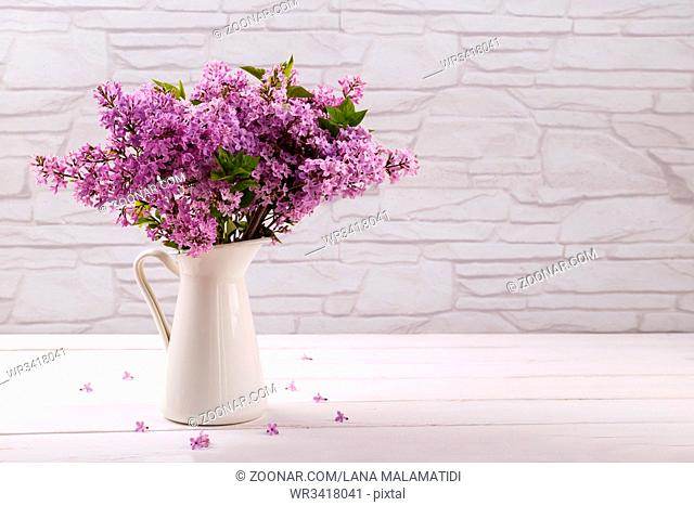 Bouquet of spring , purple lilac flowers in a pitcher on white vintage wooden table, copy space