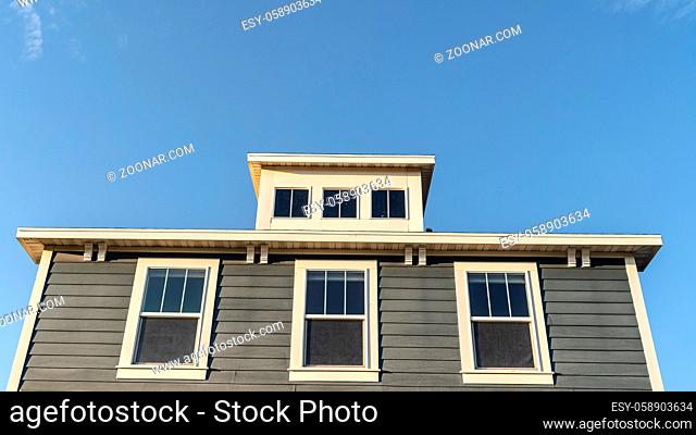 Panorama frame Grey wooden house with three upper windows matched by another three dormer windows above against a blue sky