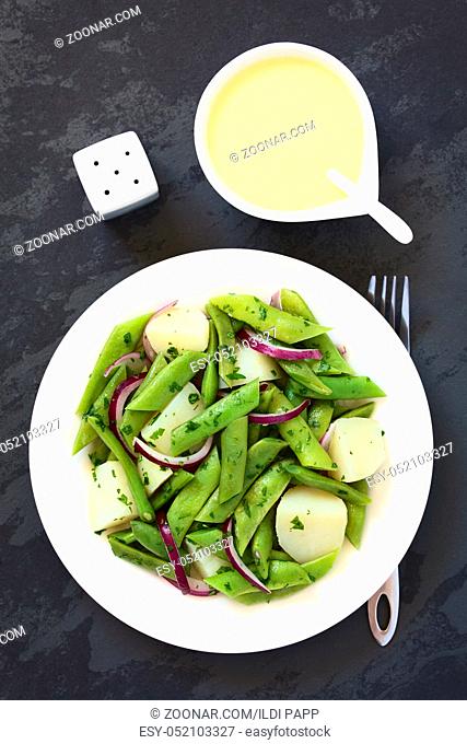 Green bean, potato and red onion salad with parsley, hollandaise sauce on the side, photographed overhead on slate with natural light