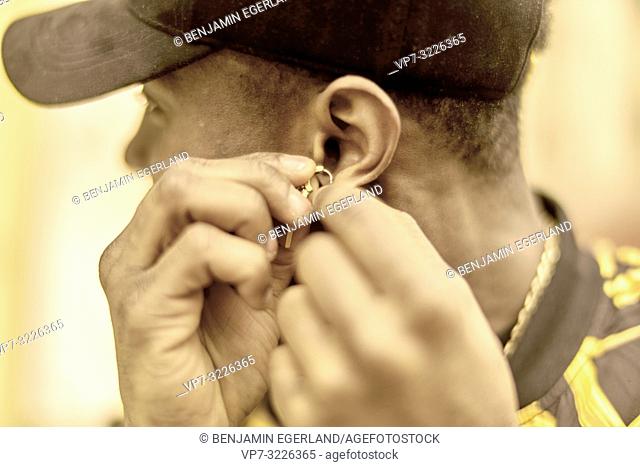 man attaching earring to left ear, in Munich, Germany