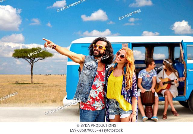 summer holidays, road trip, travel and people concept - smiling young hippie couple with friends in minivan car over african savannah background