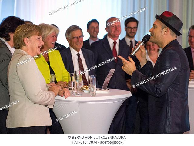 German Chancellor Angela Merkel (CDU, L) listens to a performance of singer Roger Cicero (R) during the summer celebration of the 'Verband Privater Rundfunk und...