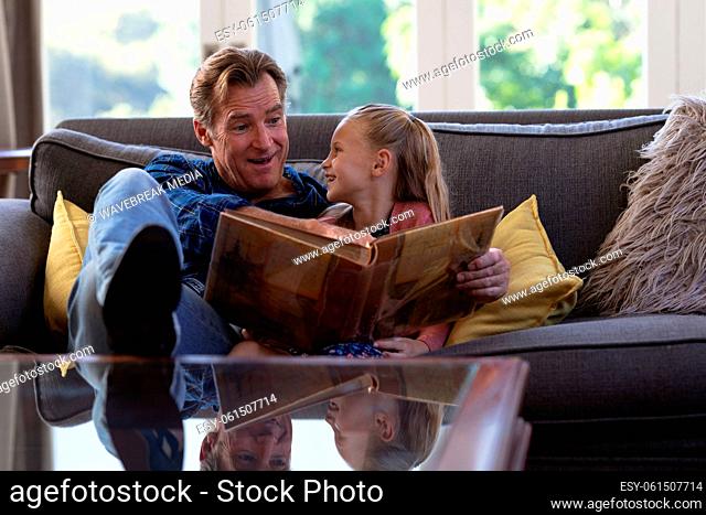 Caucasian girl and her grandfather spending time together at home sitting on a couch