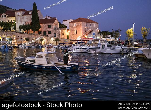 PRODUCTION - 29 September 2023, Croatia, Bol: The harbor with boats and cafes and restaurants in Bol on the island of Brac in the evening