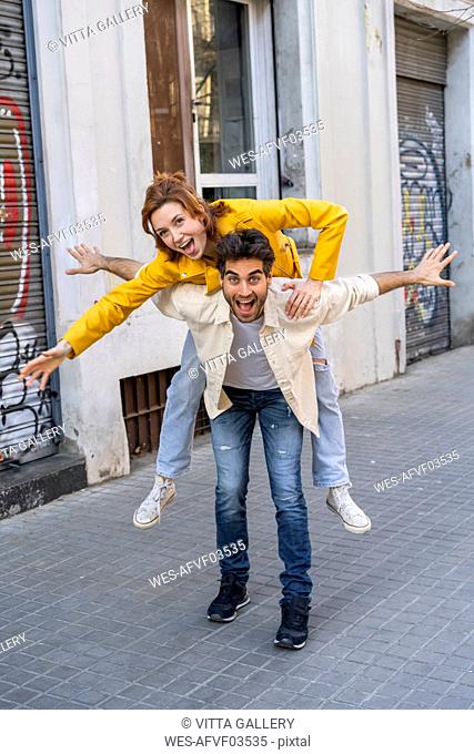 Happy man giving girlfriend a piggyback ride on pavement in the city