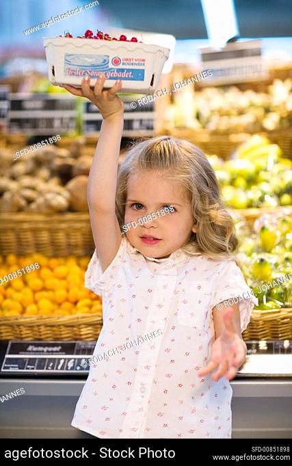 Small girl holding up a punnet of redcurrants in a supermarket