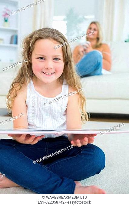 Laughing daughter with a book while her mother is resting on the sofa