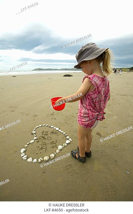 Girl exploring heart made from seashells, beach at the Moeraki Boulders, south of Oamaru, Eastcoast, South Island, New Zealand