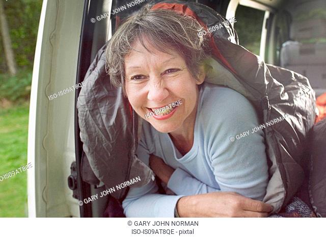 Portrait of senior woman inside sleeping bag, in open camper van